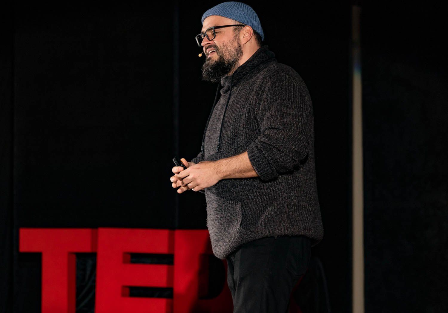 Wojciech Jachowski na scenie TEDx, w tle czerwone litery TED